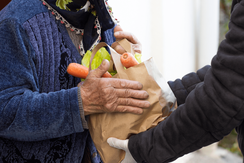 gloved hands handing a bag of groceries to an older woman