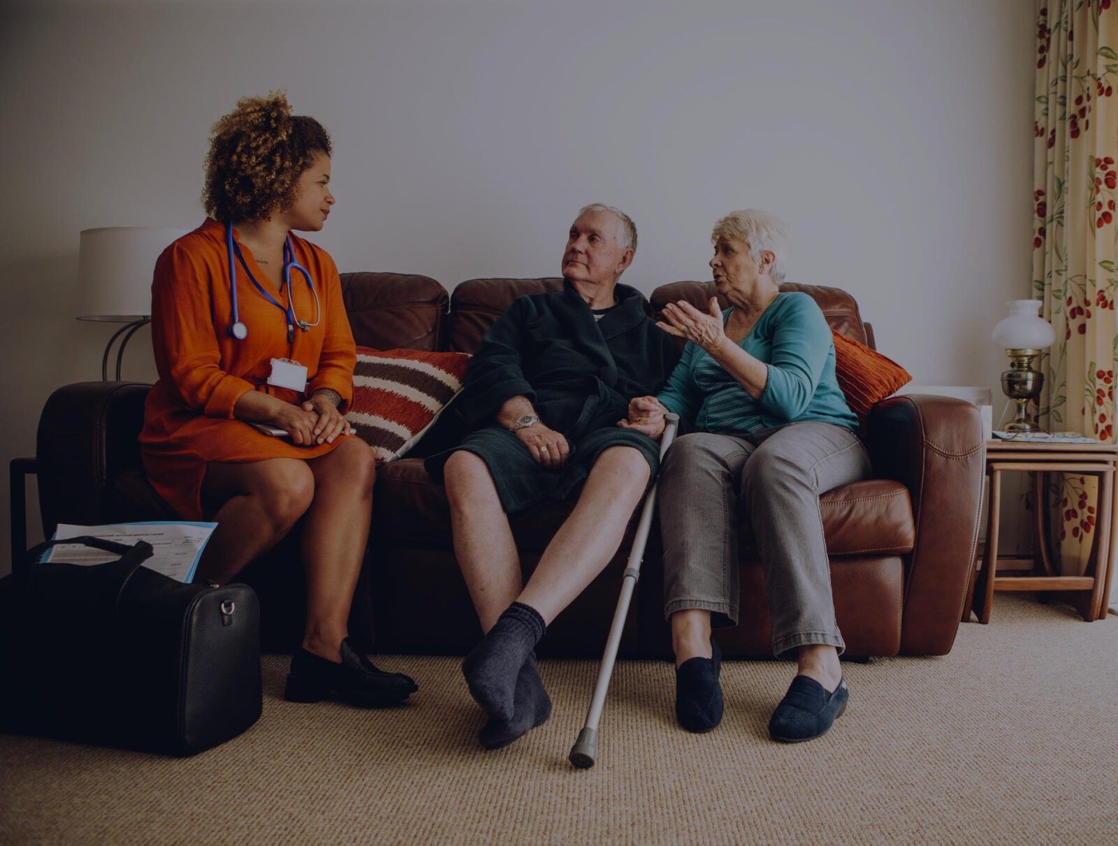 A healthcare worker conversing with an elderly couple in their living room, providing evidence-based post-procedure advice.
