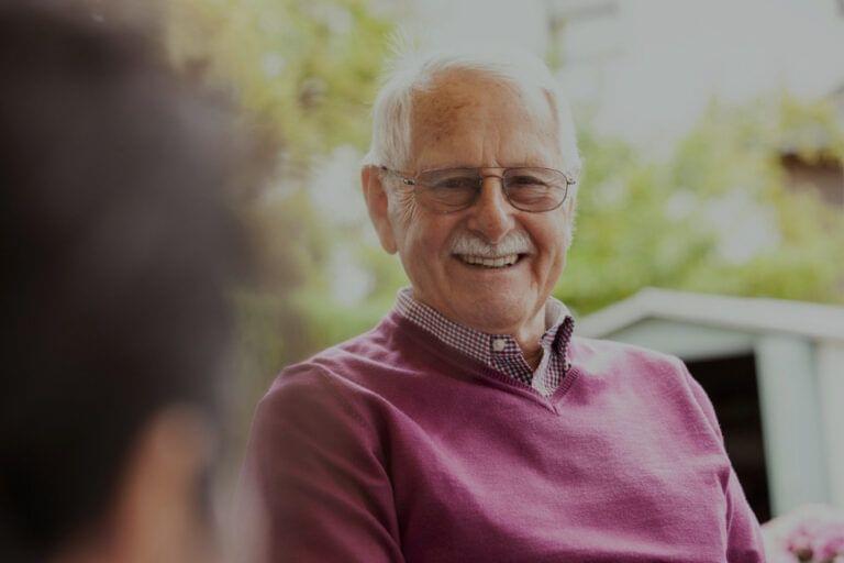 Elderly man smiling during a conversation about family caregivers outdoors.