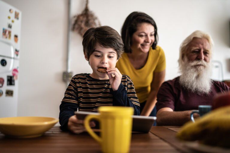 Boy using digital tablet while his mother looking for him and his grandfather at home