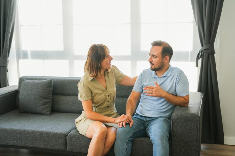 The middle-aged woman is hugging the young man sitting on the sofa in the living room of the house.