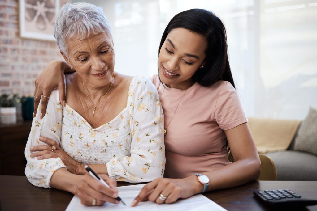 Two people are looking at a document on a table, one is writing and the other is pointing.