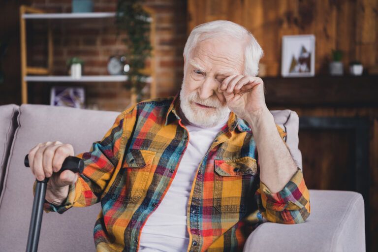 Photo of depressed stressed man pensioner wear checkered shirt holding walking cane crying sitting sofa indoors house room