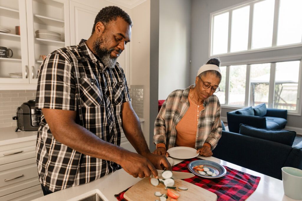 Man slicing vegetables in kitchen while woman watches with a plate