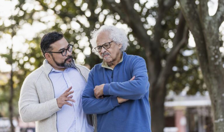 Senior Hispanic man frowning as adult son talks