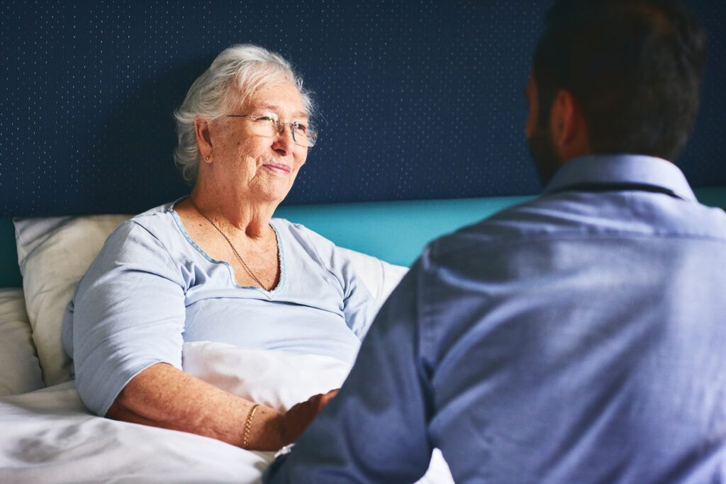 Elderly woman in bed smiling at a man seated beside her