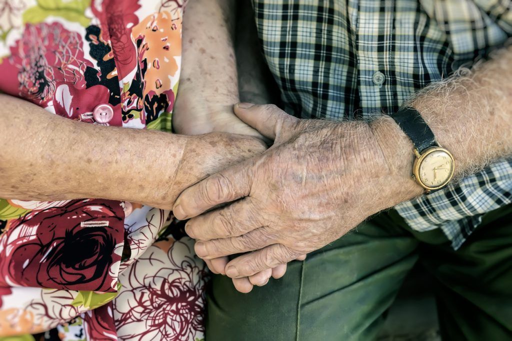Close-up of elderly couple holding hands, showing support and connection