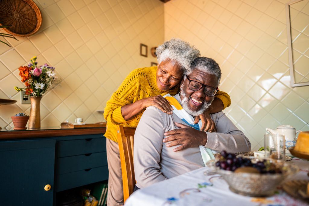Joyful elderly couple embracing and laughing together at a breakfast table