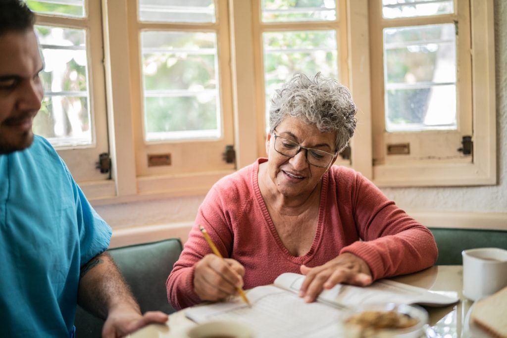 Older woman doing a puzzle book with a caregiver nearby