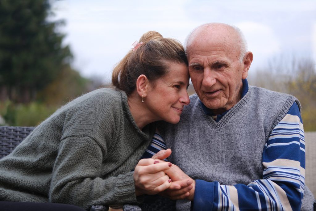 Woman sitting close to an elderly man, holding hands and sharing an affectionate moment.