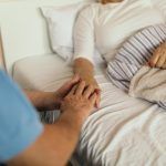 Caregiver holding the hand of a patient lying in bed, offering comfort and support.