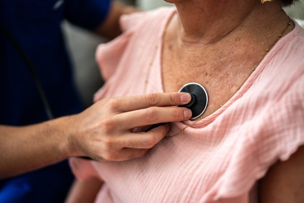 A cardiologist puts a stethoscope on an older adult woman’s chest to listen to her heart.