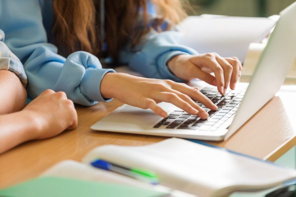 Student typing on laptop at desk with notebooks nearby