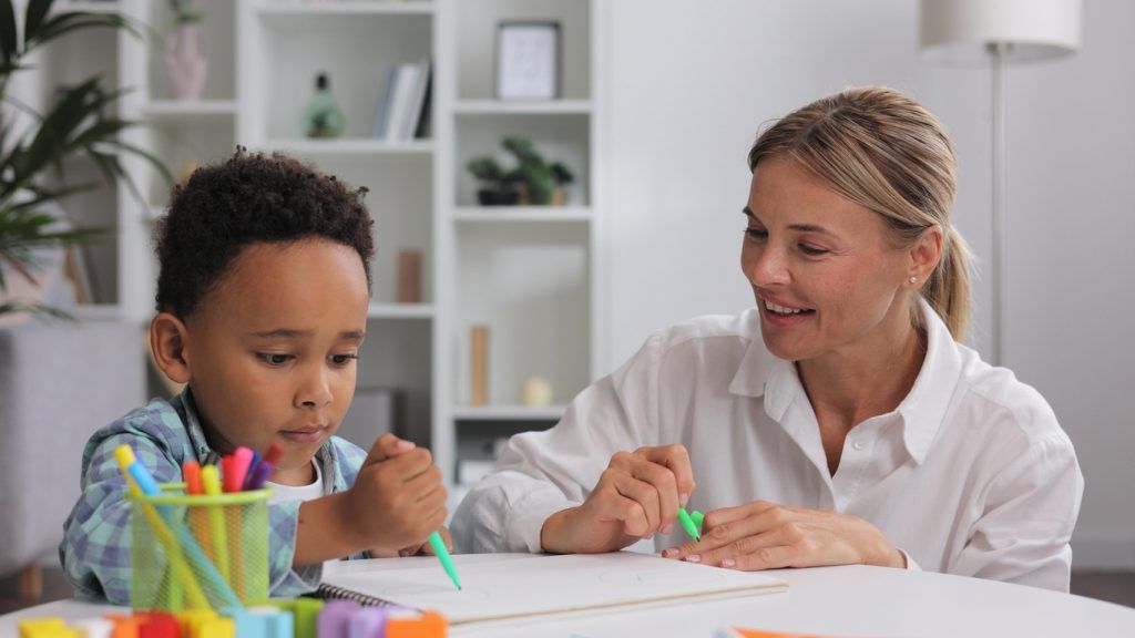 Teacher guiding child with drawing activity at table