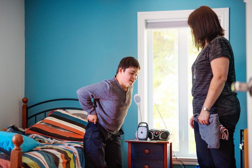 Boy with Down syndrome getting dressed with caregiver in bedroom