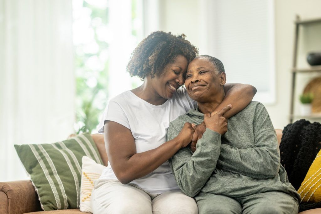 Adult daughter hugs and comforts older mother on couch