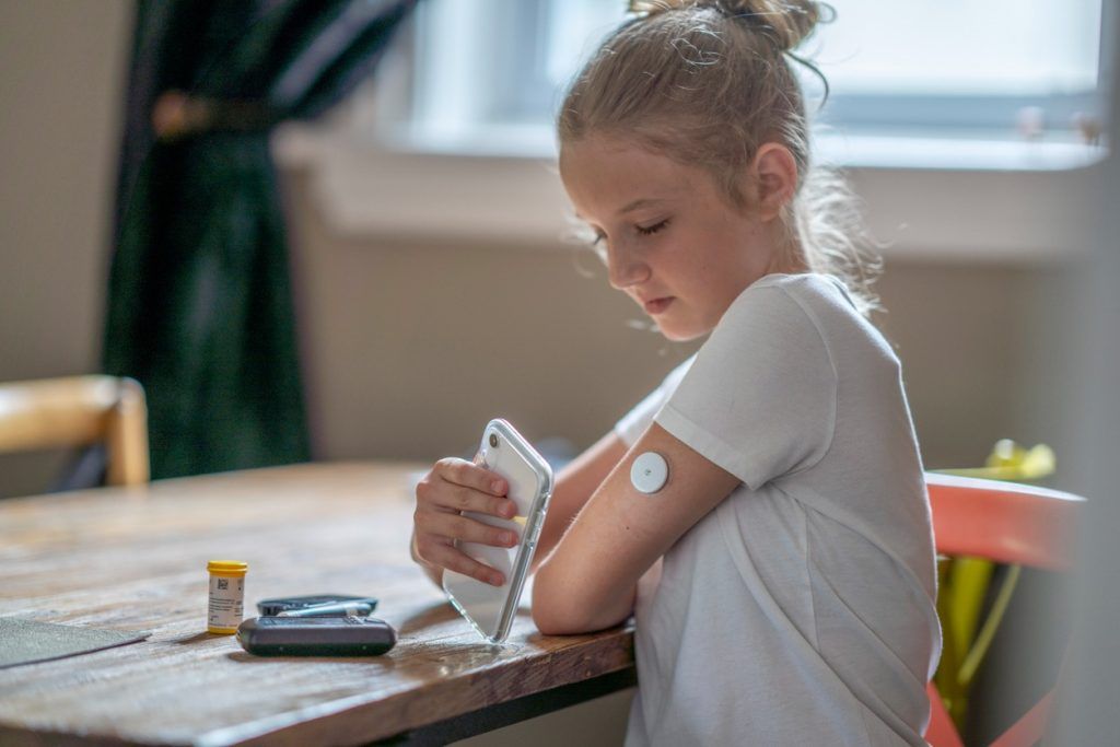 Child scans glucose monitor on arm using smartphone.