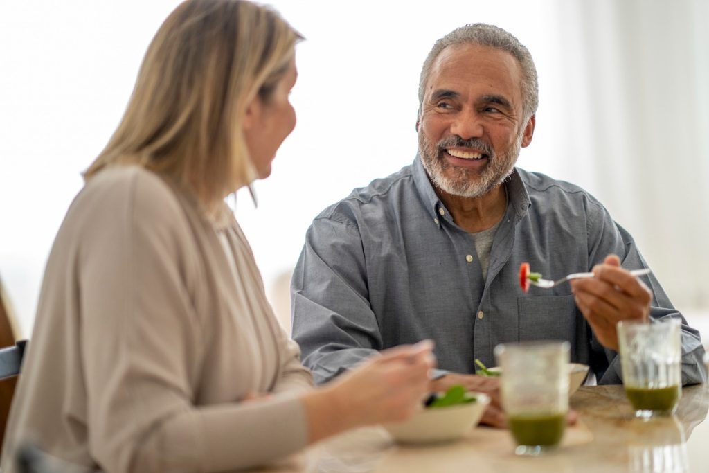 Man smiles while eating healthy meal with woman.