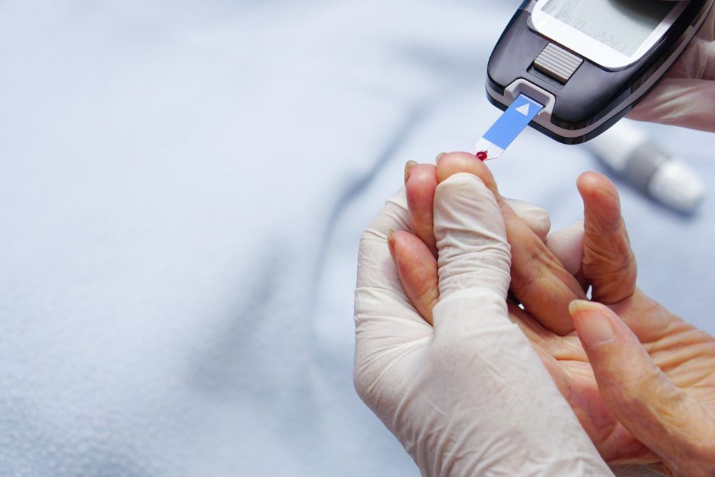 Gloved hands check blood sugar with glucose meter.