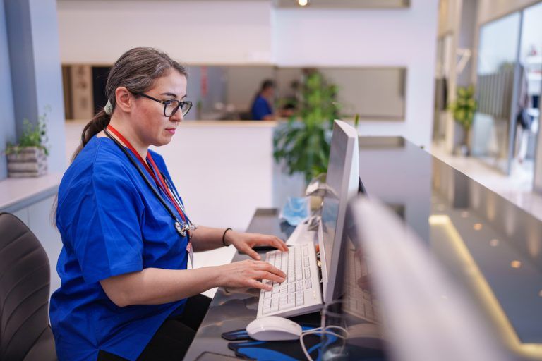 Nurse works on computer at diabetes care centre reception desk.