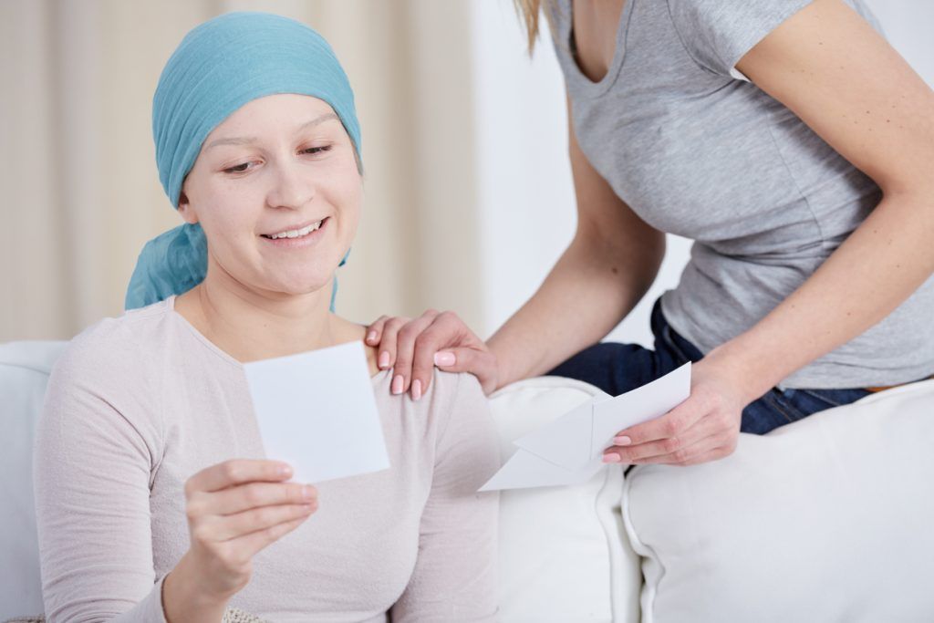Woman in headscarf smiling while reading a note with support from another person.