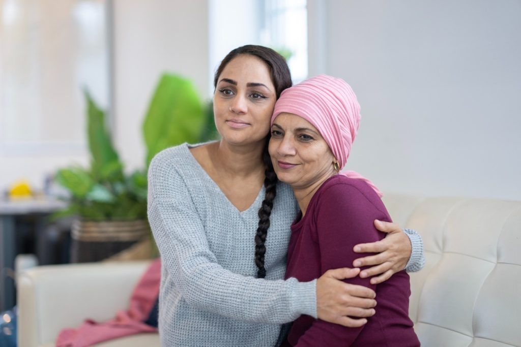 Daughter embracing her mom wearing a headscarf while sitting on a couch.