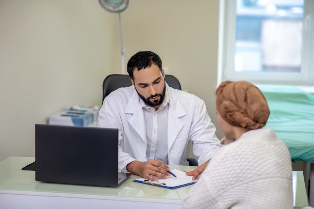 Doctor speaking with a patient wearing a headscarf during a consultation.