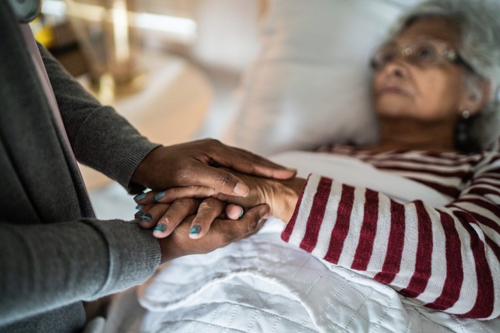 Person holding the hand of an older woman lying in bed.