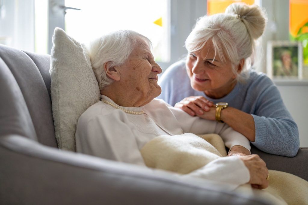 Older woman resting in a chair while caregiver leans in and comforts her