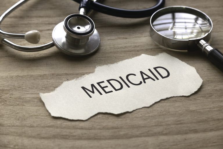 Stethoscope and magnifying glass next to paper labeled Medicaid on a desk.