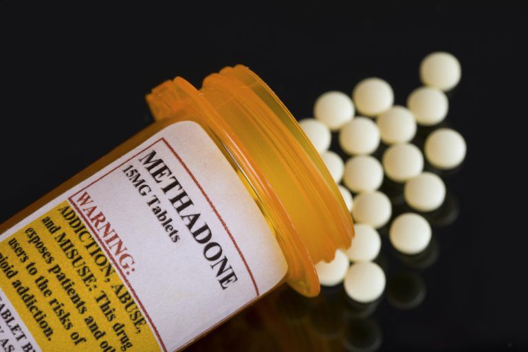 Methadone pill bottle tipped over with tablets spilling out.
