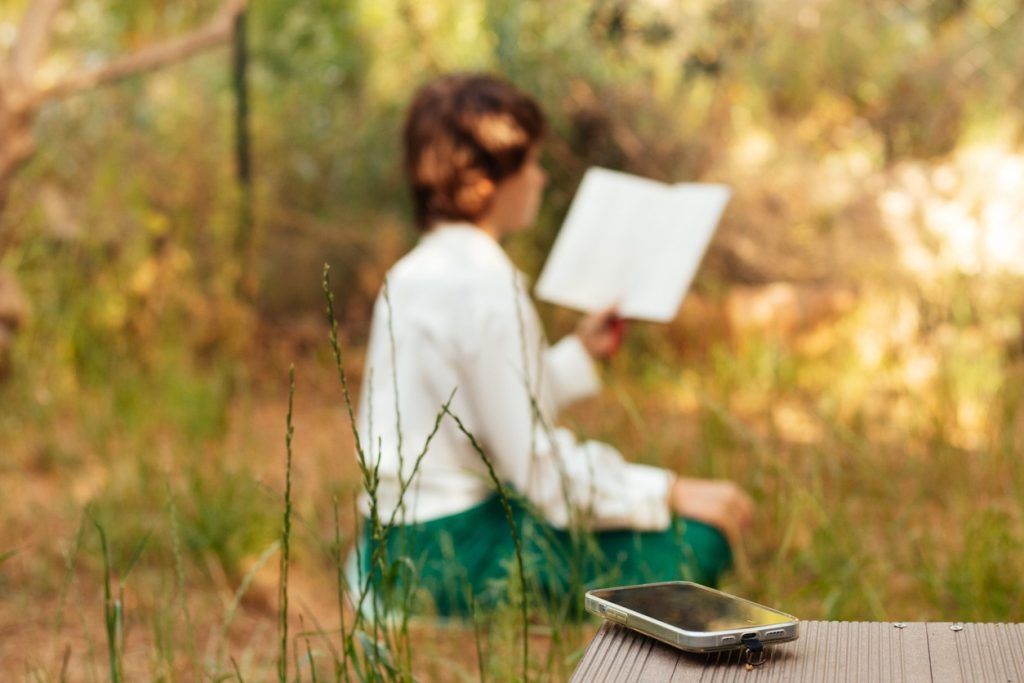 Phone on a bench with a person reading in the background.