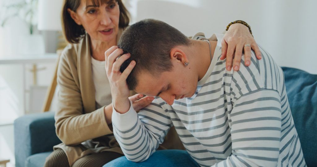 Woman comforting a distressed young man with her hand on his shoulder.